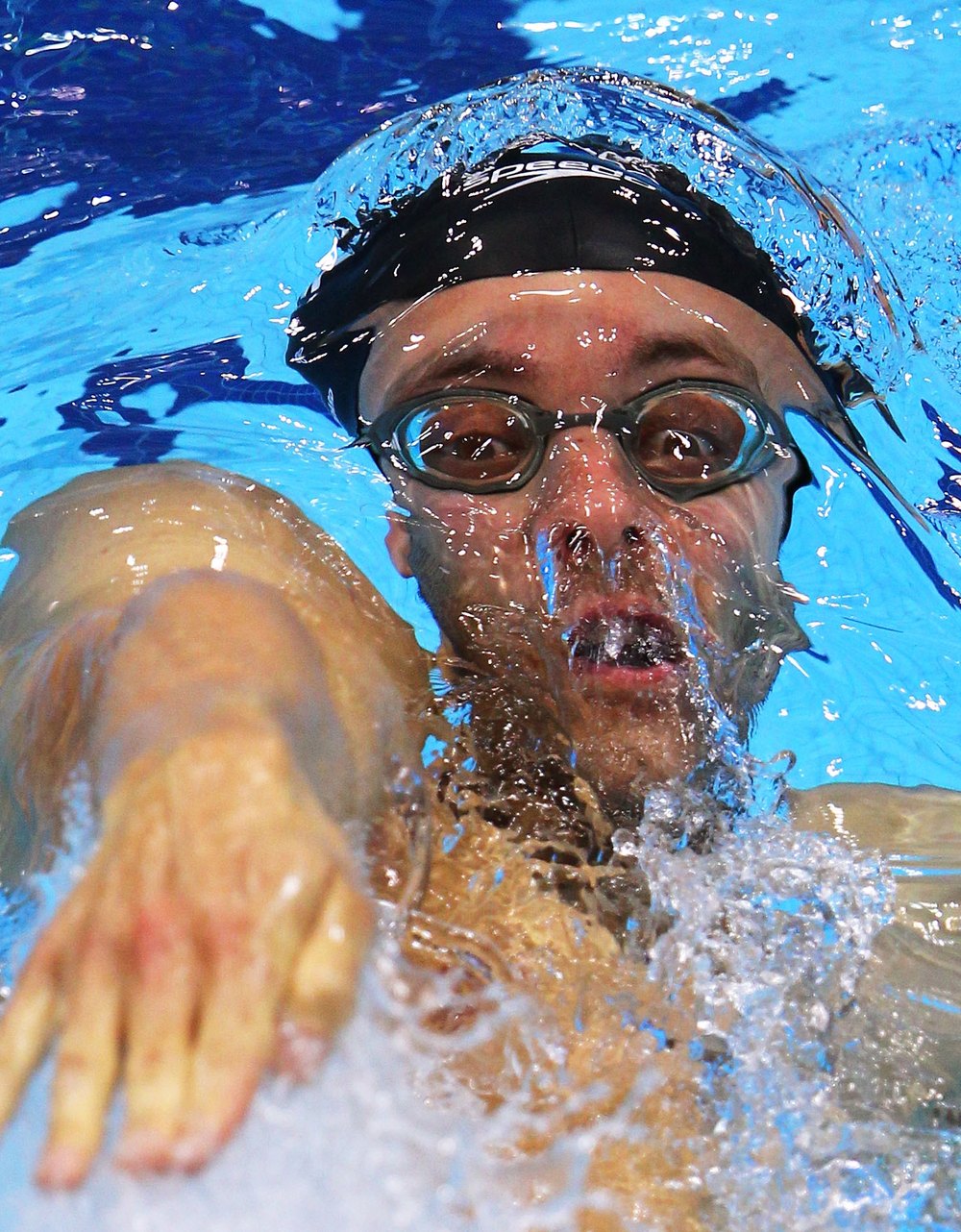 Marco Loughran crouching poolside giving front-crawl technique feedback to an adult swimmer
